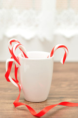 Obraz na płótnie Canvas Two candy canes in a white mug with a red ribbon for decoration