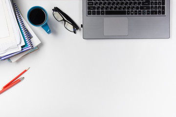 Office table desk with supplies, blank note pad, cup, pen, pc, crumpled paper, flower on white background. Top view