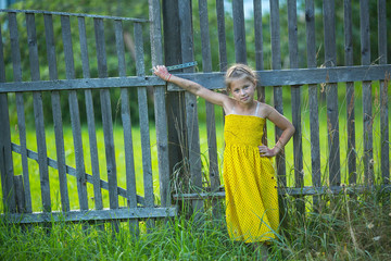 Little girl standing near fence in the village.