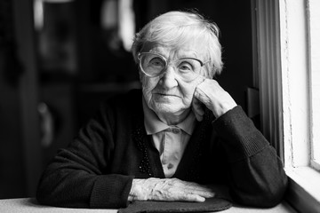 Elderly woman in glasses sitting at the table. Black and white photo.