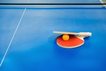 pingpong rackets and ball and net on a blue pingpong table