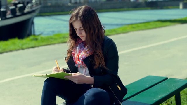 Girl writing something in her journal and smiling to the camera
