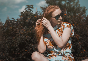 Beautiful redhead girl in the summer day outdoors with sunglasses.