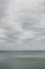 Fototapeta na wymiar Pale cloudy sky over dim greyish sea water
