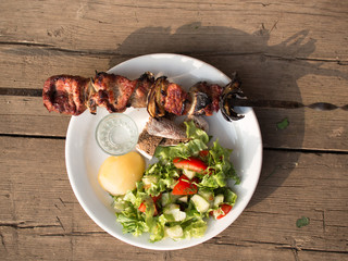 White plate with fresh vegetables, potatoes, fried meat and a shot of vodka standing on the old board