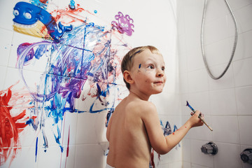Obraz premium Portrait of cute adorable white Caucasian little boy playing and painting with paints on wall in bathroom having fun, lifestyle childhood concept