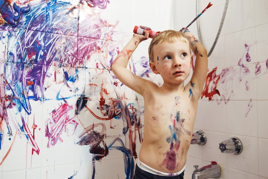 Portrait of cute adorable white Caucasian little boy playing and painting with paints  on wall in bathroom having fun, lifestyle childhood concept