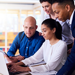 Square image of four multiethnic diverse business people all with their own fresh perspective on the information that everyone is looking at on the laptop computer and electronic tablet.