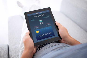 man lying sofa and holding tablet with online train ticket