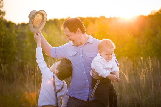Happy family walking in the park on a sunny day. Father with adorable toddler boy and cute kid boy having fun on a summer meadow.  Sunset in the park. Outdoors. Parent with children Together.