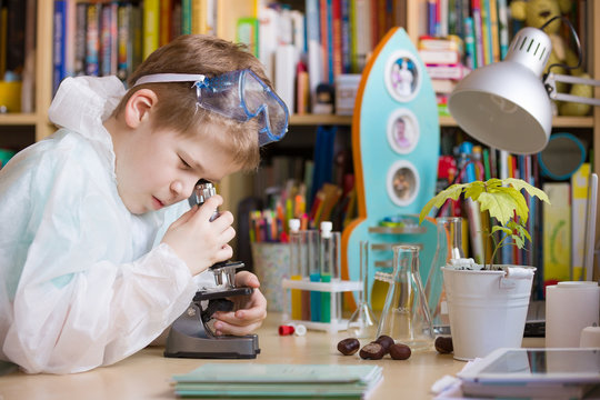 Cute elementary school boy looking into microscope at his desk at home. Young scientist making experiments in his home laboratory. Indoors. Child and science.
