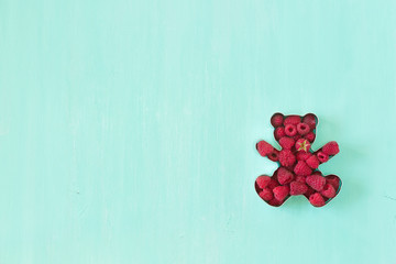 Teddy bear shaped mold for the cookies full of fresh organic raspberries on turquoise background.