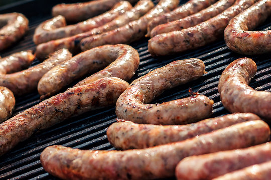 BBQ with fiery sausages on the grill. Red baked delicious juicy sausages in row. Tasty sausage preparing on a barbecue grill over charcoal in outdoor. 