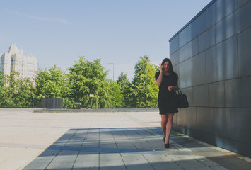business girl in black dress near the wall talking on the phone