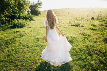 Young girl in a white dress in the meadow. Woman in a beautiful long dress posing in the garden....