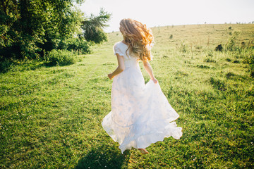 Young girl in a white dress in the meadow. Woman in a beautiful long dress posing in the garden. Stunning bride in a wedding dress