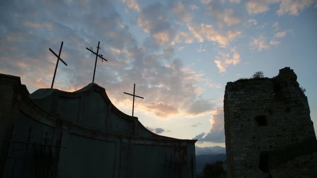 Tilt from the ground to the sky with a silhouette of three Catholic crosses and a Medieval Tower  at the Sunset.
