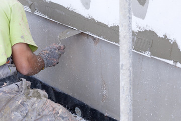Workers spreading mortar over styrofoam insulation and mesh with trowel
