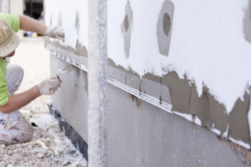 Workers spreading mortar over styrofoam insulation and mesh with trowel