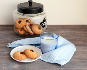 Cookies in glass jar and on plate and a glass of milk - healthy breakfast. Wooden table, cotton napkin, tissue.