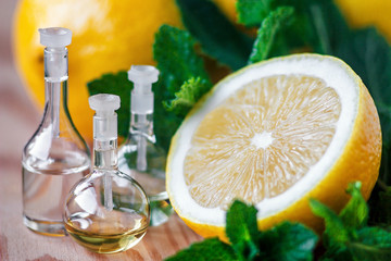 Essential oil in glass bottle with fresh, juicy lemon fruit and green leaves of mint on wooden...