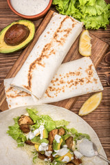 Chicken, avocado and vegetables burrito on the wooden background.