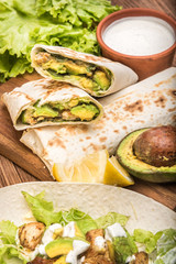 Chicken, avocado and vegetables burrito on the wooden background.