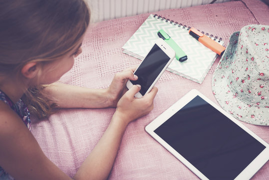 Girl using smartphone indoors on her room on bed