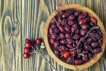 Rosehips in a wooden bowl on a wooden surface. Rosa canina hips.