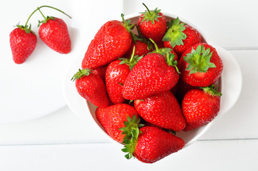 Strawberries in a white bowl on white boards a top view. Bright food
