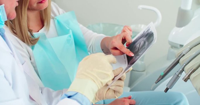 Dentist holding x-ray image of teeth and explaining his young female patient her dental problems