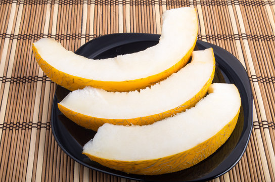 Three slices of juicy yellow melon on a black plate