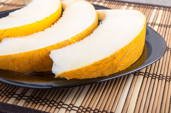 Slices of juicy yellow melon on a black plate closeup