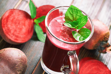 Beetroot juice with mint leaves and beetroots scattered around on wooden background
