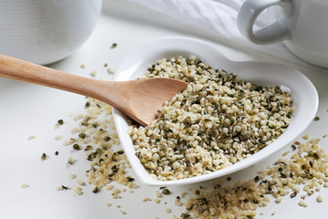 Hemp seeds in heart shaped ceramic bowl and wooden spoon on white background