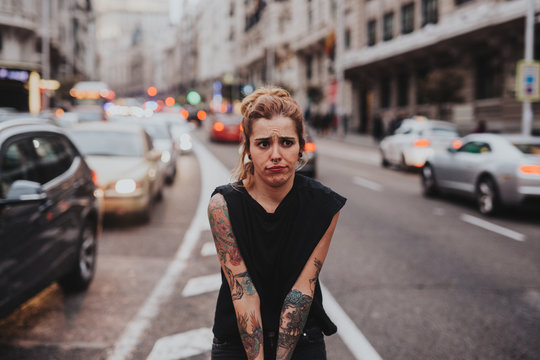 Tattooed blonde girl making faces while standing in the middle of road