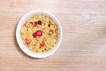 Cereal with strawberry in white bowl on wooden table