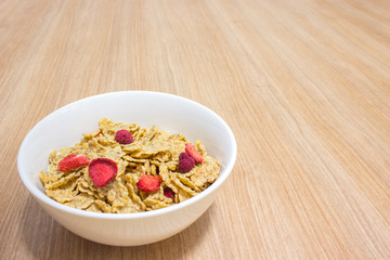 Cereal with strawberry in white bowl on wooden table