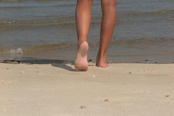 Woman walking on sand beach leaving footprints in the sand.