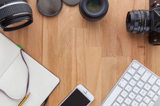 top view of a desktop of a photographer consisting on a camera, a keyboard, a smart phone and a tablet on a wooden desk background 