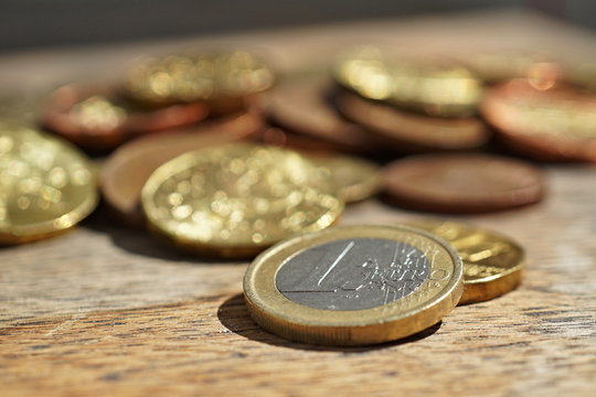 Macro detail of a pile of coins on the wooden surface with a silver and golden Euro coin separated from other metallic coin currencies 