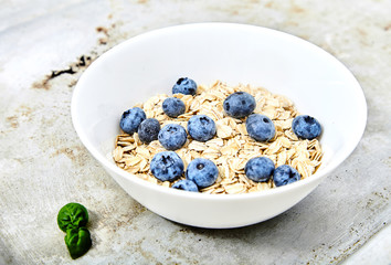 Raw oat flakes topped blueberries in white bowl