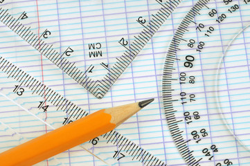 Rapporteur, équerre, règle graduée et crayon posés sur une feuille de papier