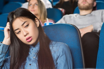 Waste of my time! Young beautiful asian female looking away bored sitting at the movie theatre