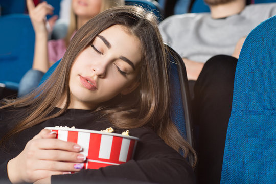 Taking a nap. Closeup shot of a gorgeous young woman sleeping holding her popcorn bucket at the movie theatre
