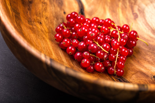 Bunch of red currants in a bowl from walnut wood. Selective focus.