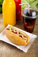 Hotdog with ketchup and mustard with cola on the wooden plank