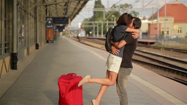 Happy couple embracing on railway station platform. Farewell at the train station, young girl and guy kissing on platform