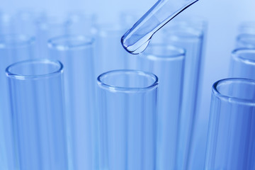 Close up of a pipette dropping a  sample into a test tube on blue background