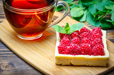 Raspberry cake with a cup of tea on the wooden background with mint leaves